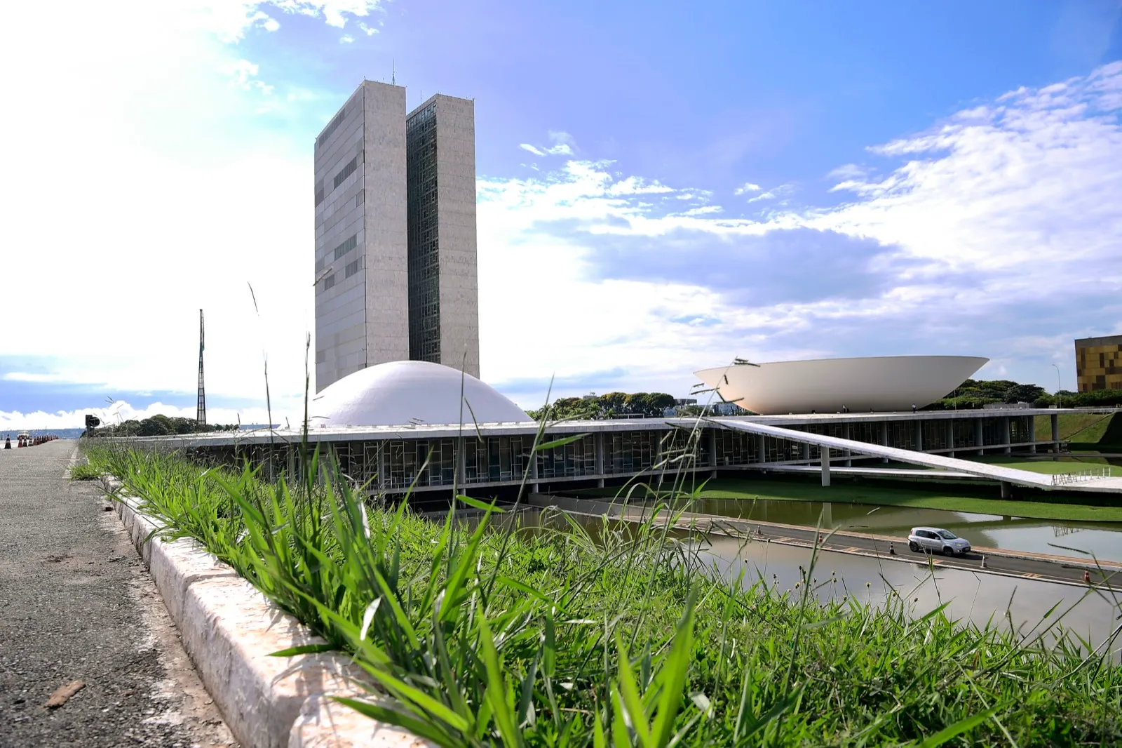 Palácio do Congresso Nacional visto de lado, com as duas torres, a cúpula do Senado e a cúpula invertida da Câmara, sob céu azul.