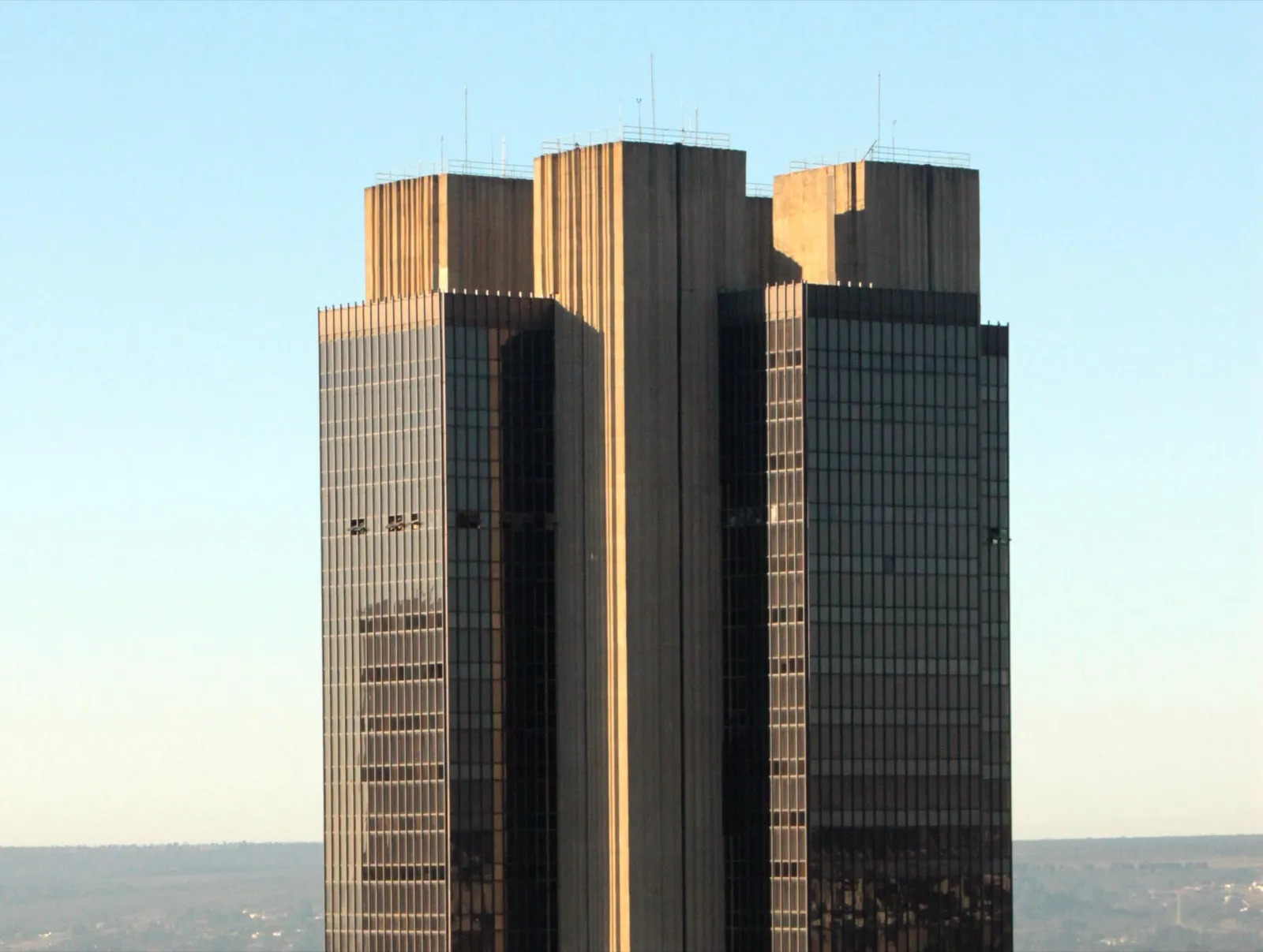 Fachada do edifício-sede do Banco Central do Brasil em Brasília, com torre de concreto e vidro sob céu azul.