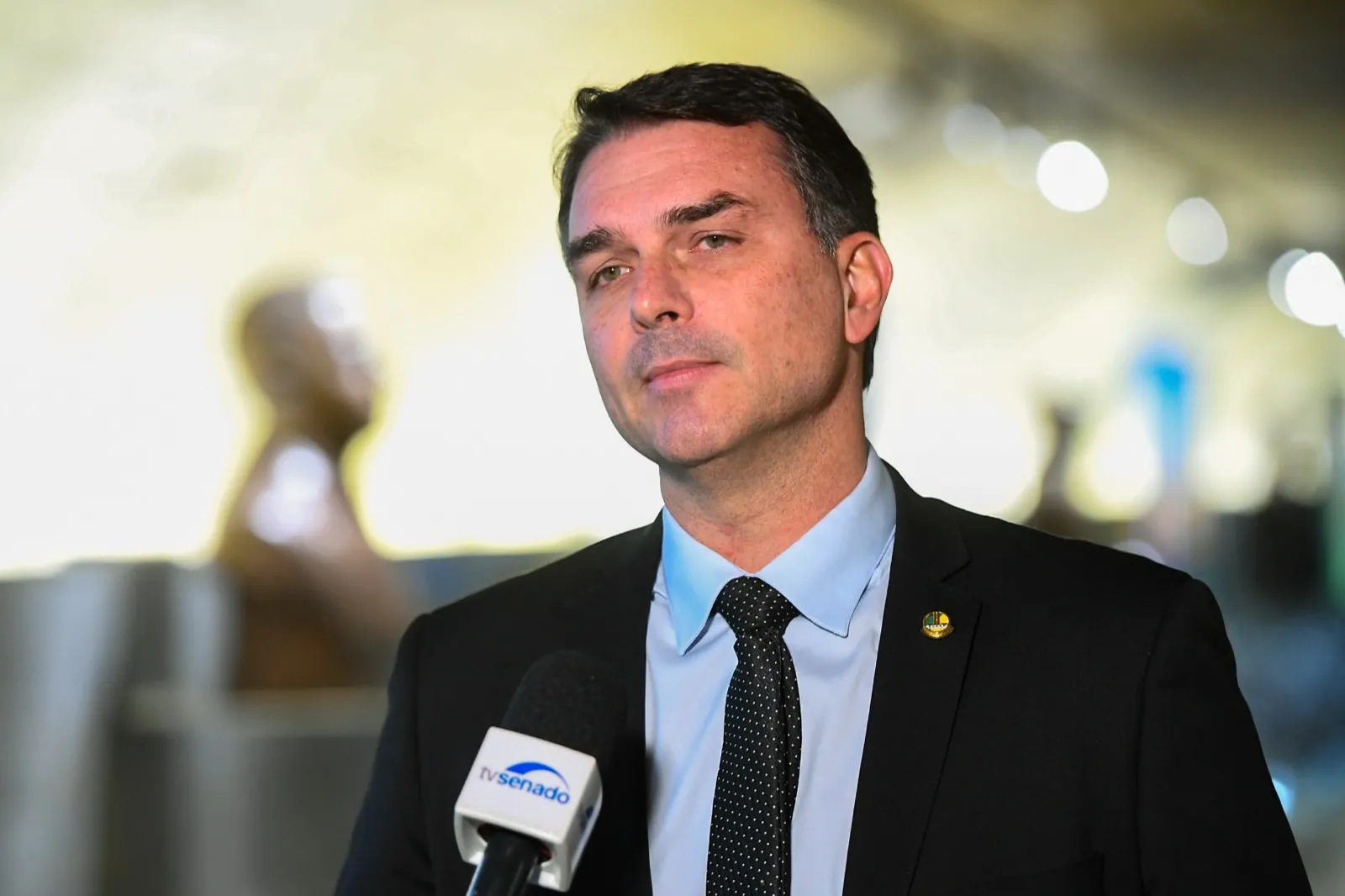 O senador Flávio Bolsonaro, de terno, fala durante entrevista no Senado.