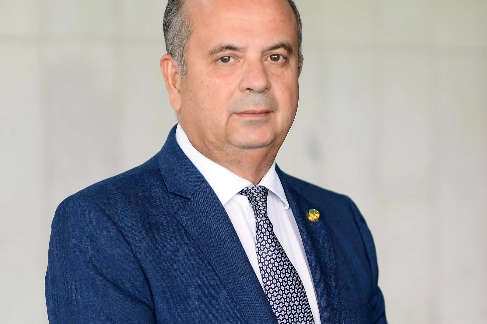 Retrato do senador Rogério Marinho, de terno azul, camisa branca e gravata estampada, diante de fundo claro.