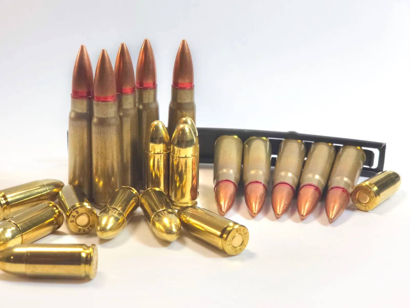 Cartuchos de munição de calibres 9 mm e 7,62 x 39 mm, alguns em pé e outros deitados, sobre fundo branco.