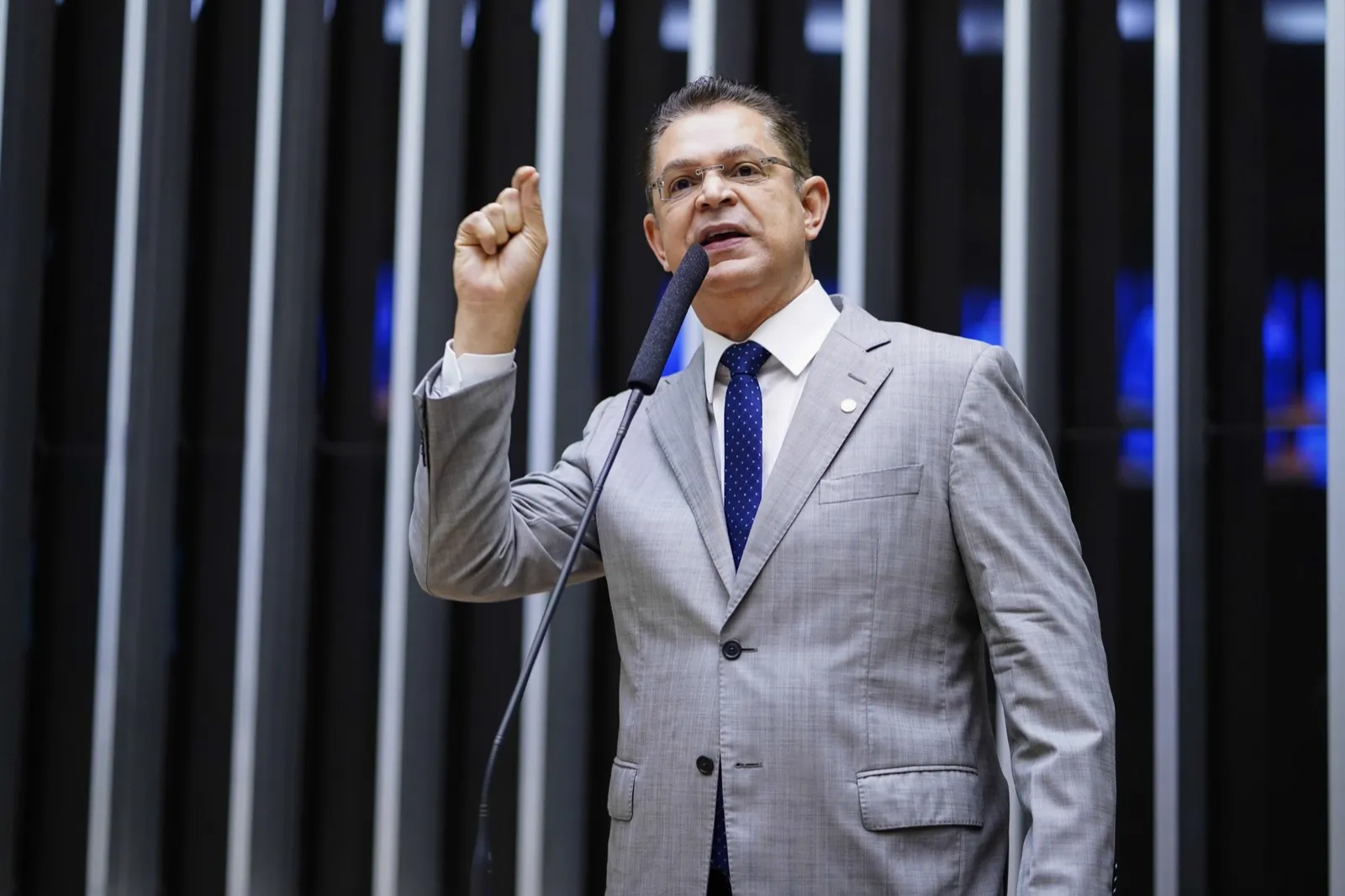 O deputado Sóstenes Cavalcante discursa de pé ao microfone, de terno cinza e com o punho erguido, na Câmara dos Deputados.