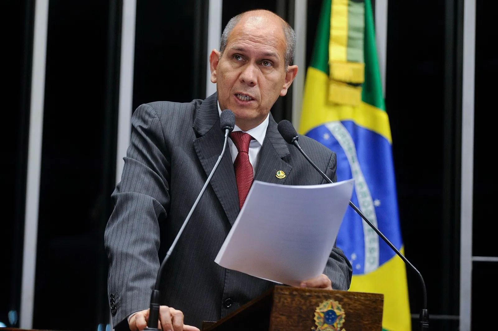 Um parlamentar discursa no púlpito do Plenário do Senado Federal, com a bandeira do Brasil ao fundo.