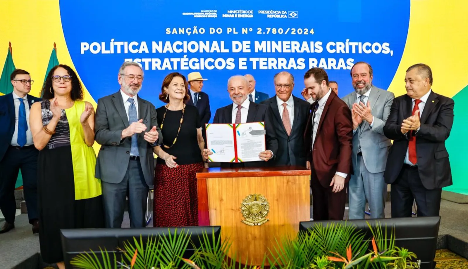Lula segura o documento assinado da sanção, cercado por ministros e autoridades que aplaudem, diante de um painel com o título da política de minerais críticos.