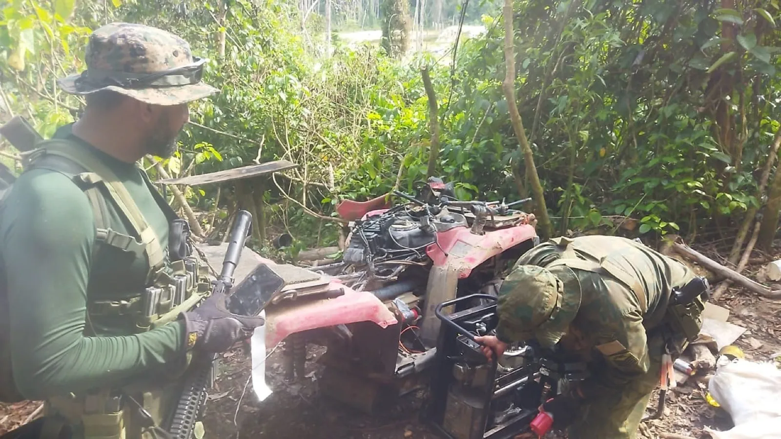 Dois militares examinam equipamentos apreendidos em área de mata durante operação na fronteira norte.