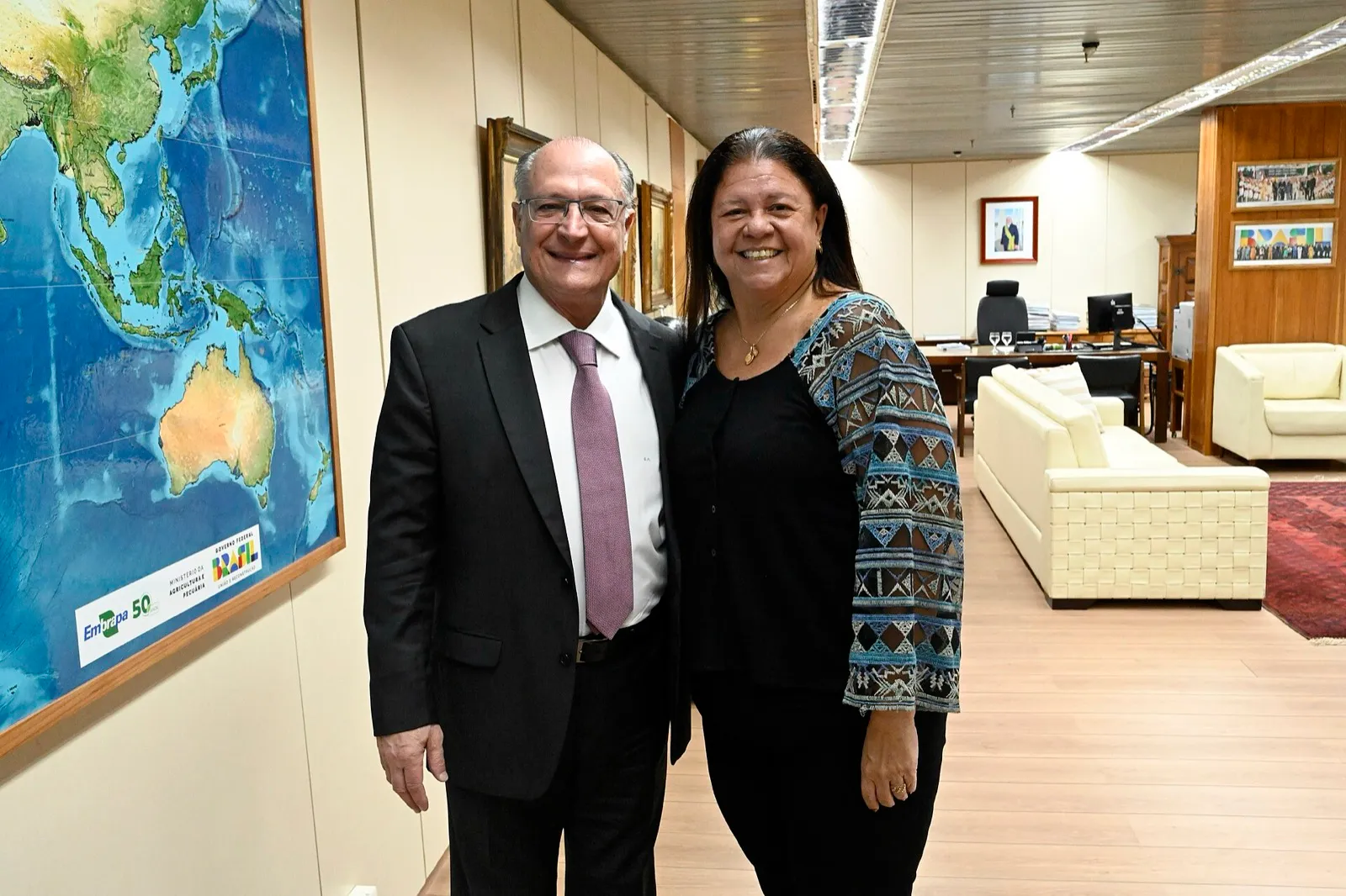 Laura Carneiro e Geraldo Alckmin posam em um gabinete ao lado de um mapa-múndi.