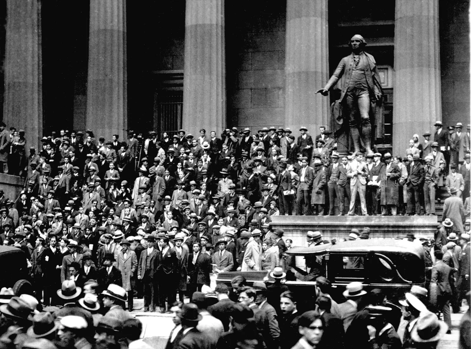 Multidão de homens de chapéu e terno reunida nos degraus de um prédio de colunas de pedra, em Nova York, com a estátua de George Washington à direita.