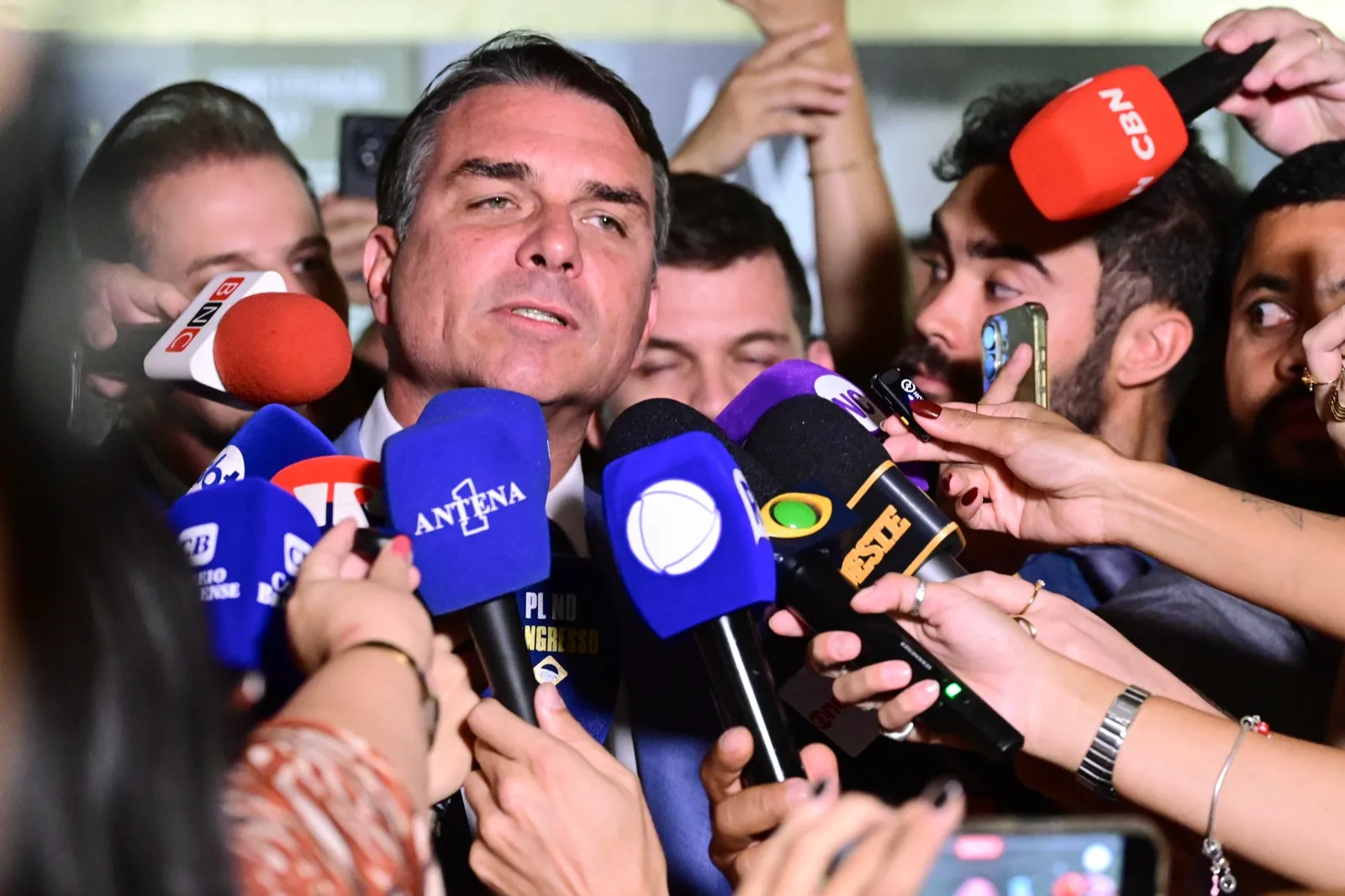O senador Flávio Bolsonaro fala a jornalistas cercado de microfones de emissoras de rádio e televisão, no Senado Federal.