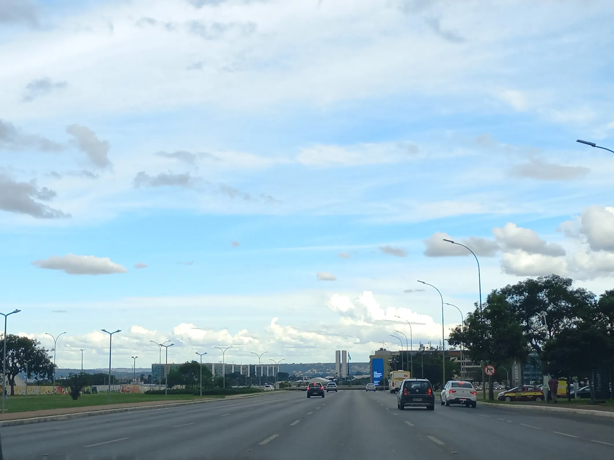 Avenida larga e quase sem trânsito sob céu azul, com as duas torres do Congresso Nacional ao fundo, no horizonte, em Brasília.