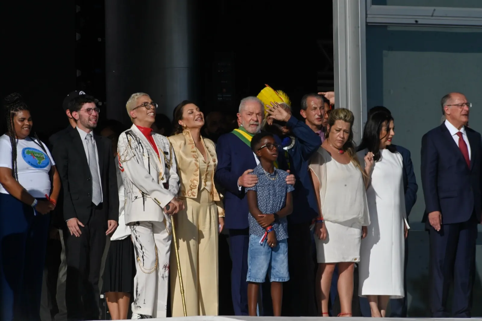 Homem de terno azul e faixa presidencial abraça um menino, cercado por um grupo de pessoas em uma plataforma durante a cerimônia de posse de 2023.