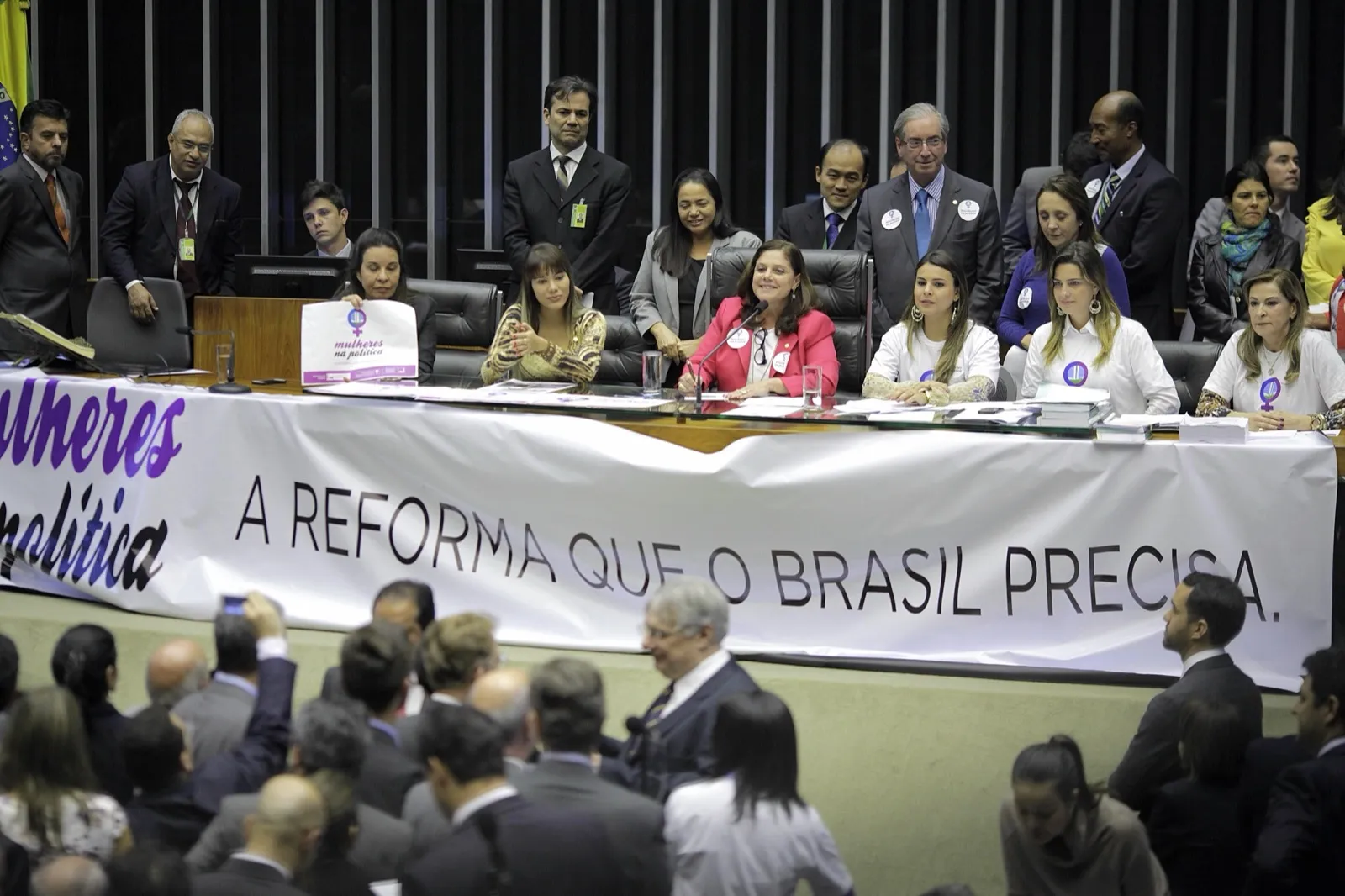 Plenário da Câmara dos Deputados com parlamentares sentados à mesa, atrás de uma faixa branca com a frase “A reforma que o Brasil precisa”.