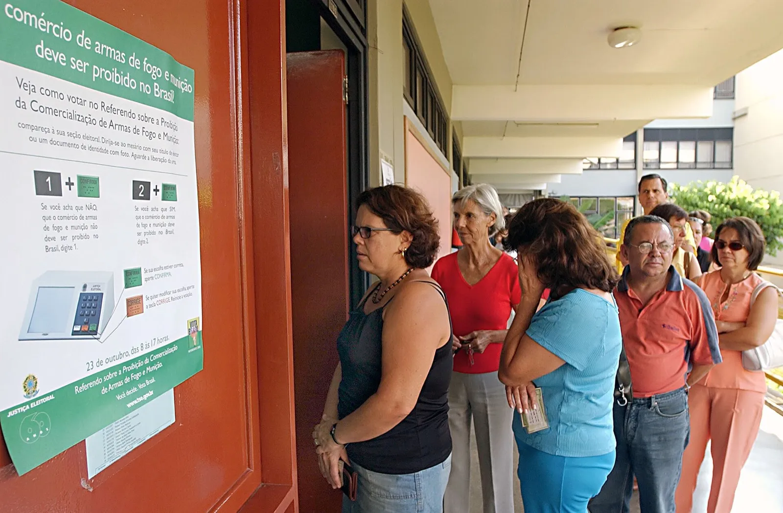Eleitores aguardam em fila ao lado de cartaz com instruções para o referendo sobre armas de 2005.
